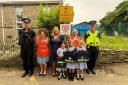 The administrator and head of Breage C of E Primary School with their Hi Vis  jackets and children showing off their book bag stickers, joined by Tri Service safety and  neighbourhood police officers, and Diana Thomas, of Breage Parish Council